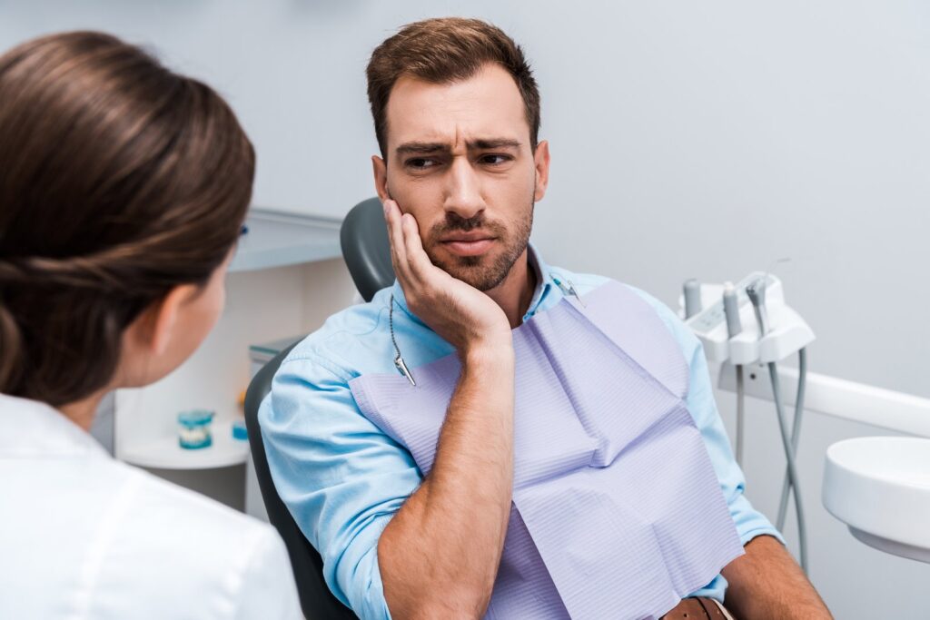 Dental patient holding jaw in pain, showing signs of a toothache that may be a dental emergency