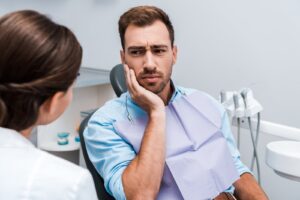 Dental patient holding jaw in pain, showing signs of a toothache that may be a dental emergency